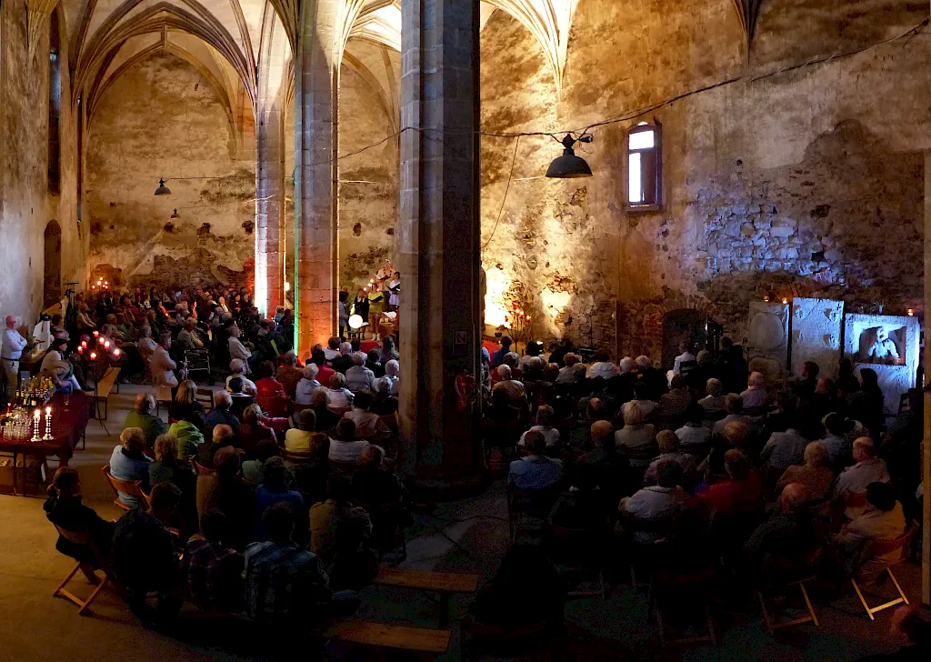 Voll besetztes Kirchenschiff bei einem Konzert: Publikum zwischen den gotischen Pfeilern, die Steinwände warm angestrahlt